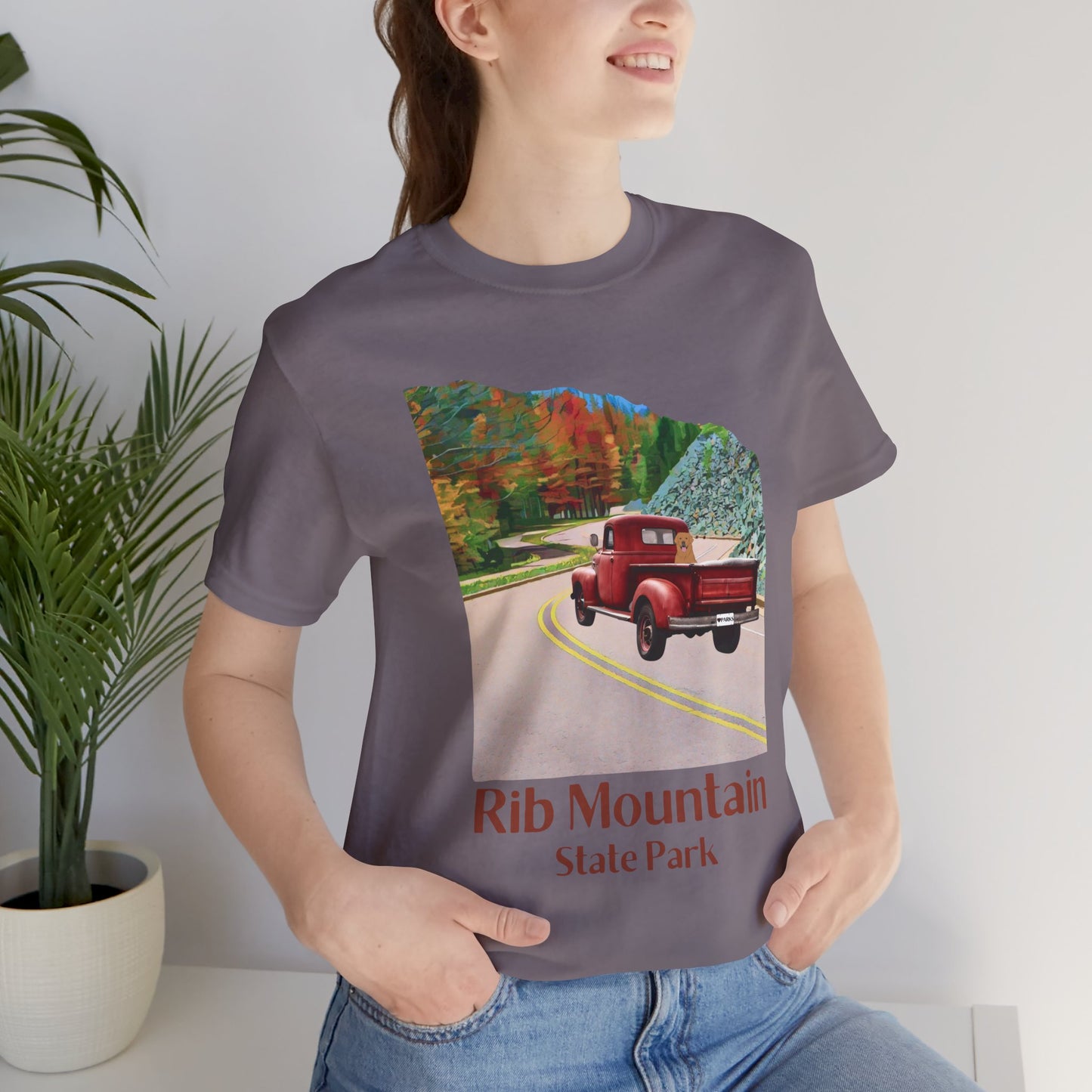 Female model wearing storm grey colored T-shirt with vintage truck driving up the road to Rib Mountain State Park during fall leaf color graphic.