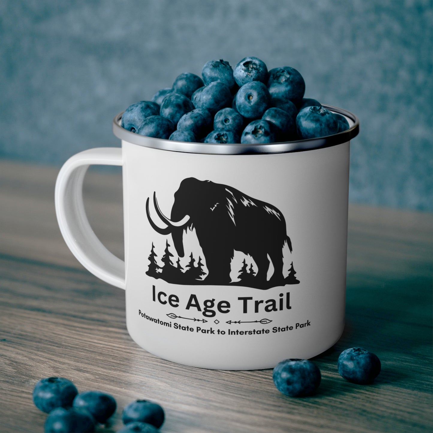 White enamel Ice Age Trail camper mug with silver lip. Features a depict of a mammoth and the text “Ice Age Trail, Potawatomi State Park to Interstate State Park”.