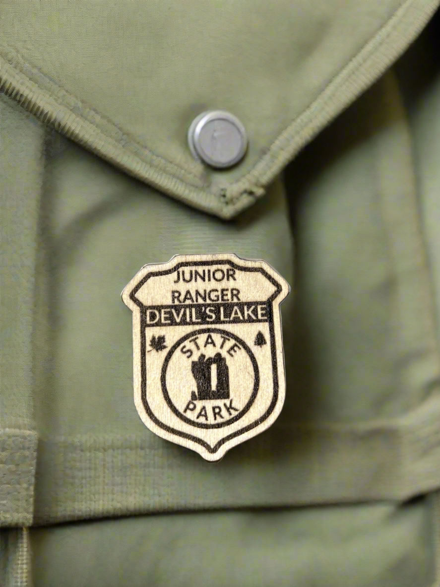 Wood badge shaped junior ranger pin with text Devil's Lake State Park and Devil's Doorway symbol.