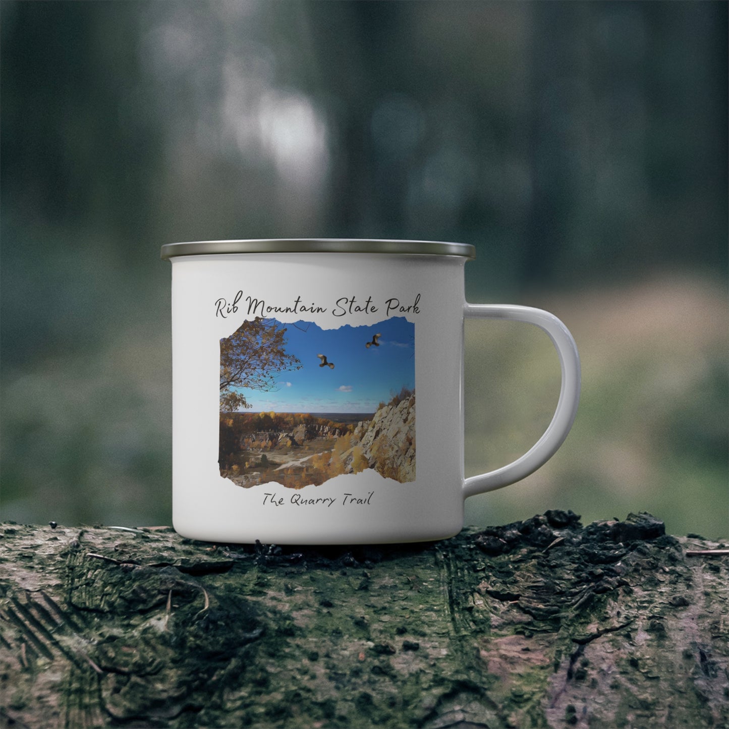 White enamel camper mug with a quarry scene printed on it with the text: Rib Mountain State Park, The Quarry Trail. Background: cup sitting on a log.