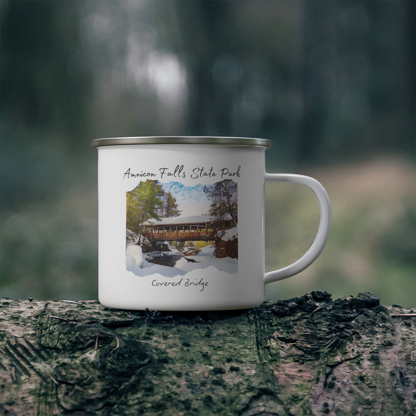 White enamel mug depicting the covered bridge at Amnicon Falls State Park in winter. Background: mug sitting on a log.