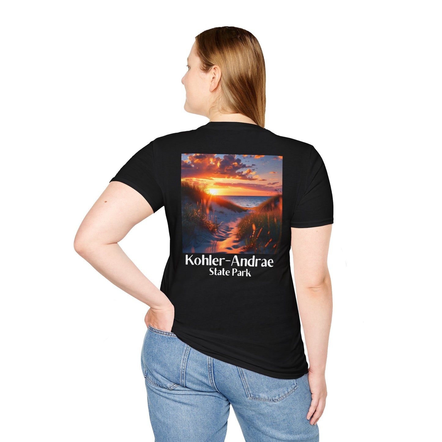 Female model wearing a black t-shirt featuring a back design of looking through the sand dunes at a colorful sunrise over Lake Michigan and the text: Kohler-Andrae State Park.