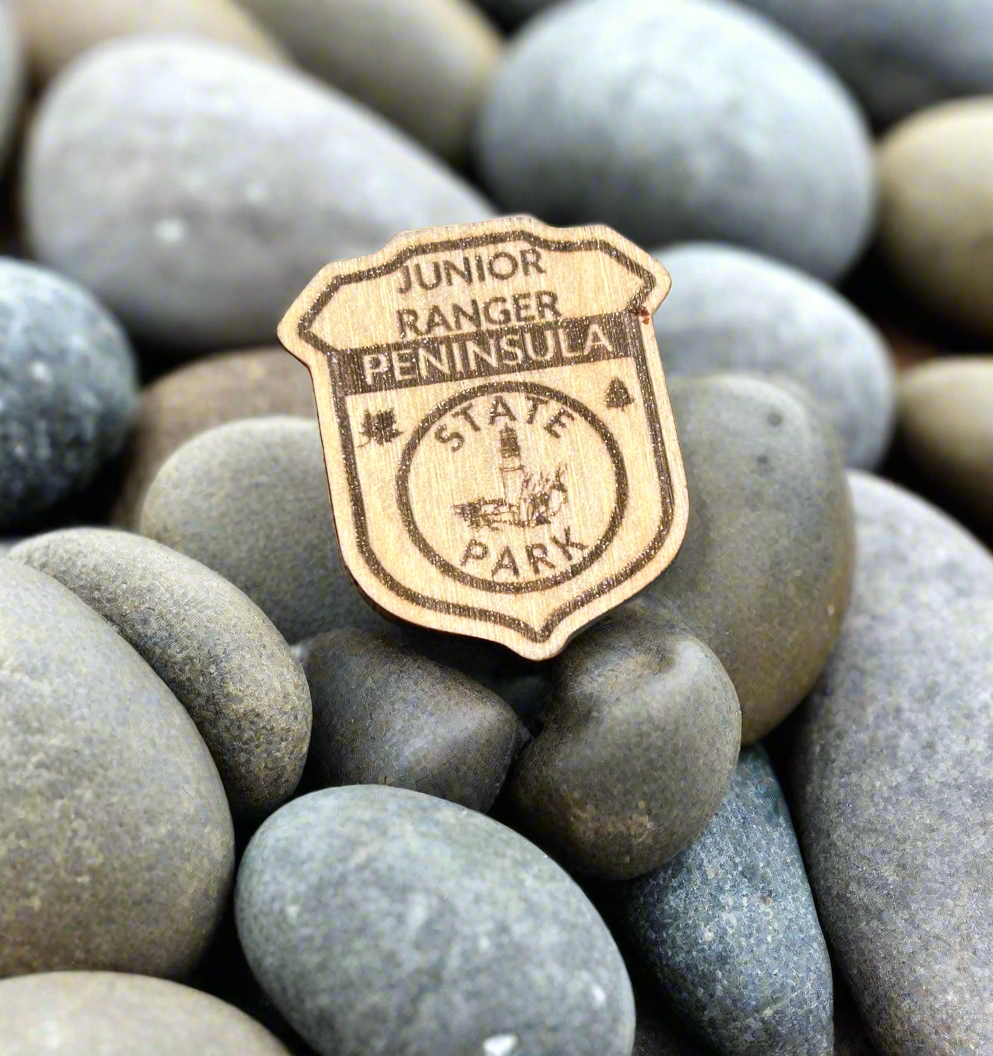 Wood badge shaped junior ranger pin with text Peninsula State Park and a lighthouse icon.