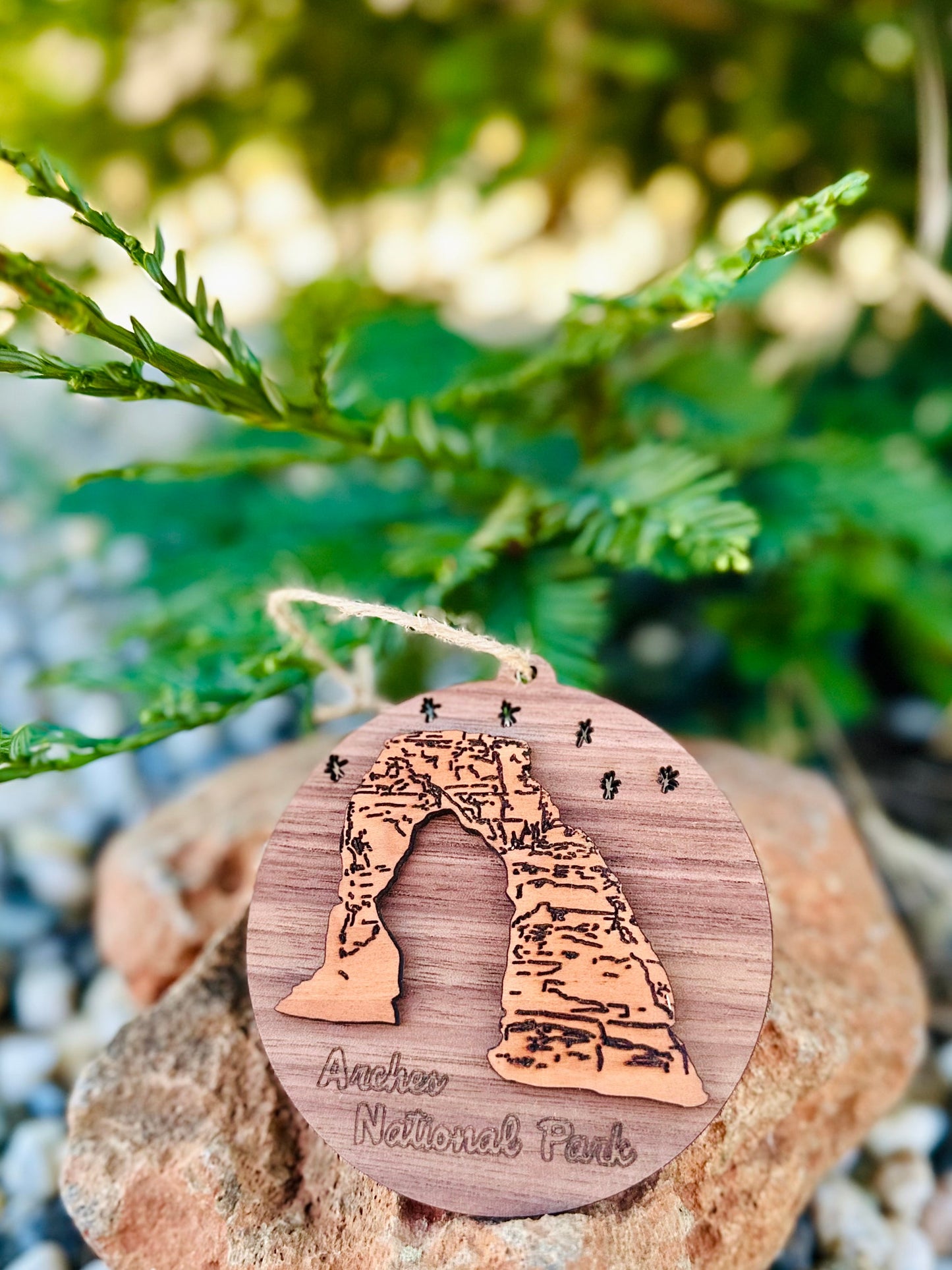 Wooden ornament with Arches National Park design on a rock with greenery in the background