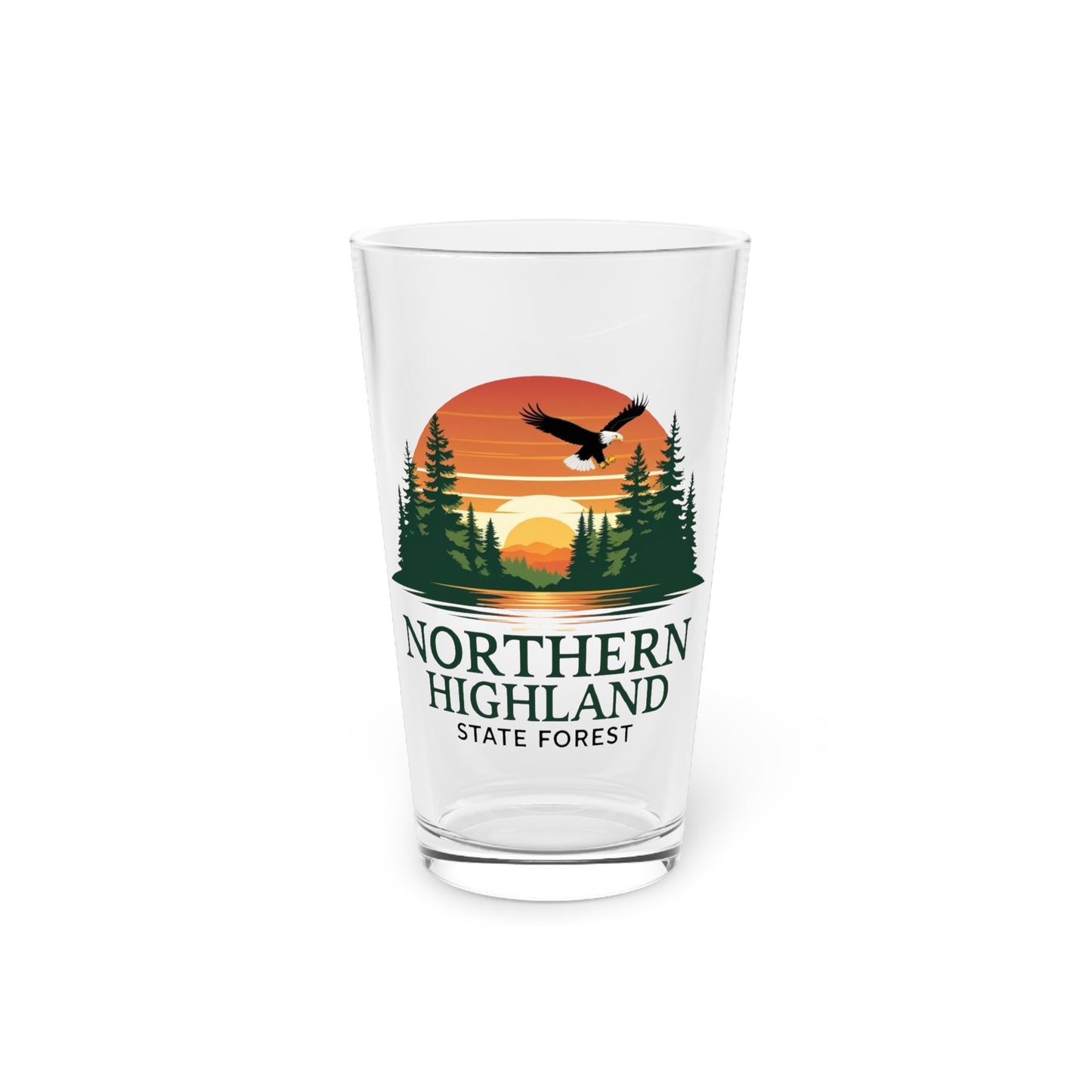16 oz glass pint featuring a colorful design of a sunset over a lake surrounded by pine trees and a Bald Eagle Soaring overhead, with the text Northern Highland State Forest.
