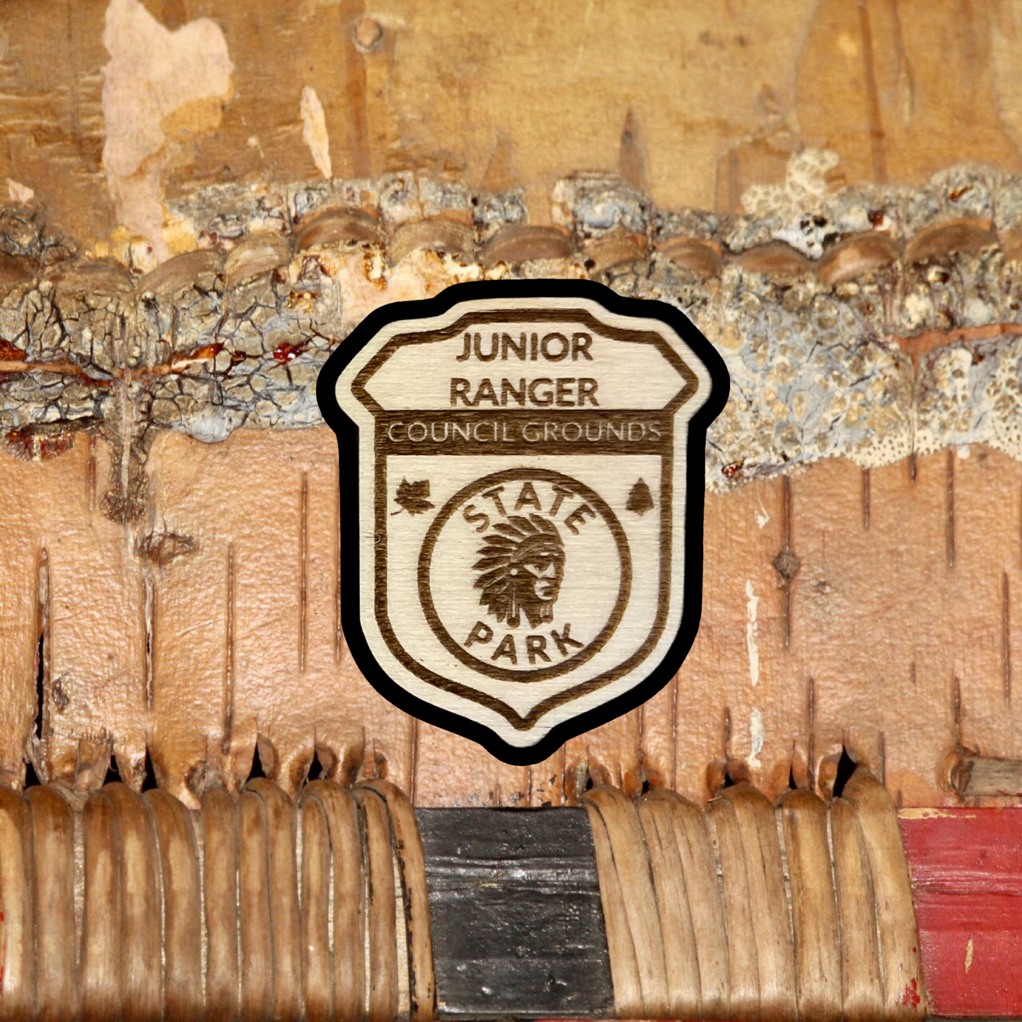 Wood badge shaped JR Ranger Badge with the text “Junior Ranger, Council Grounds State Park” with a Indian Head symbol. Photo background: handmade birch product.