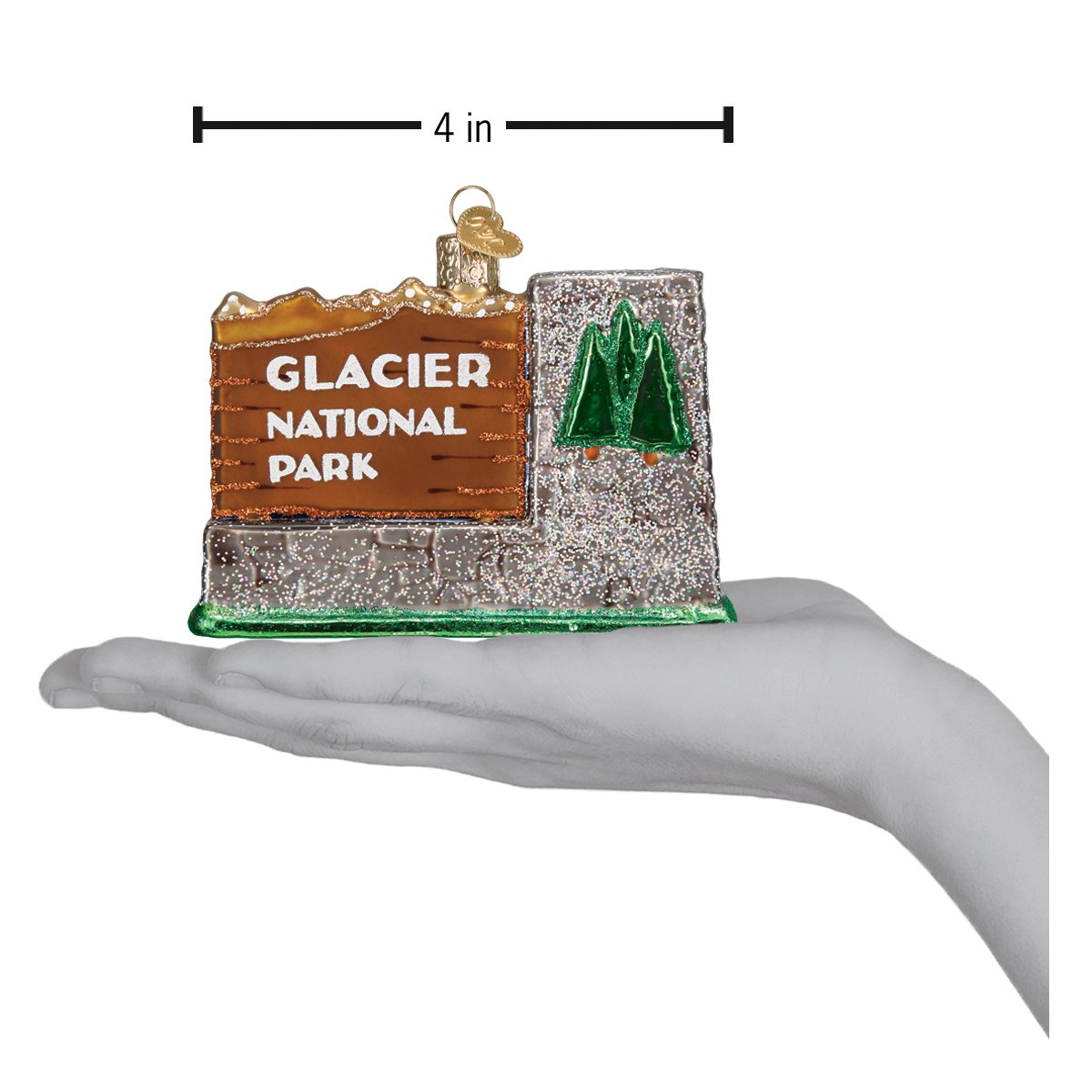 3-D glass ornament in the shape of the glacier national Park entrance sign in a hand to show dimensions, against a white background