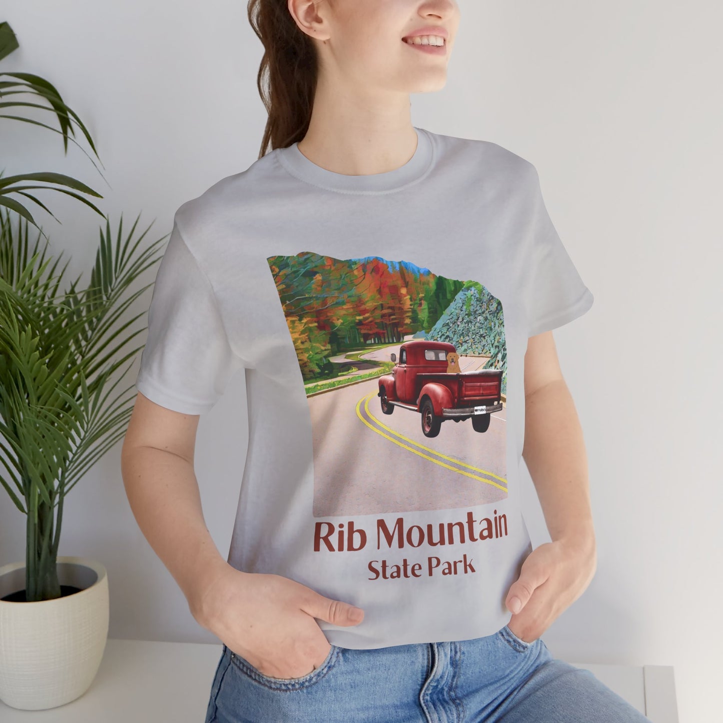 Female model wearing athletic grey colored T-shirt with vintage truck driving up the road to Rib Mountain State Park during fall leaf color graphic.