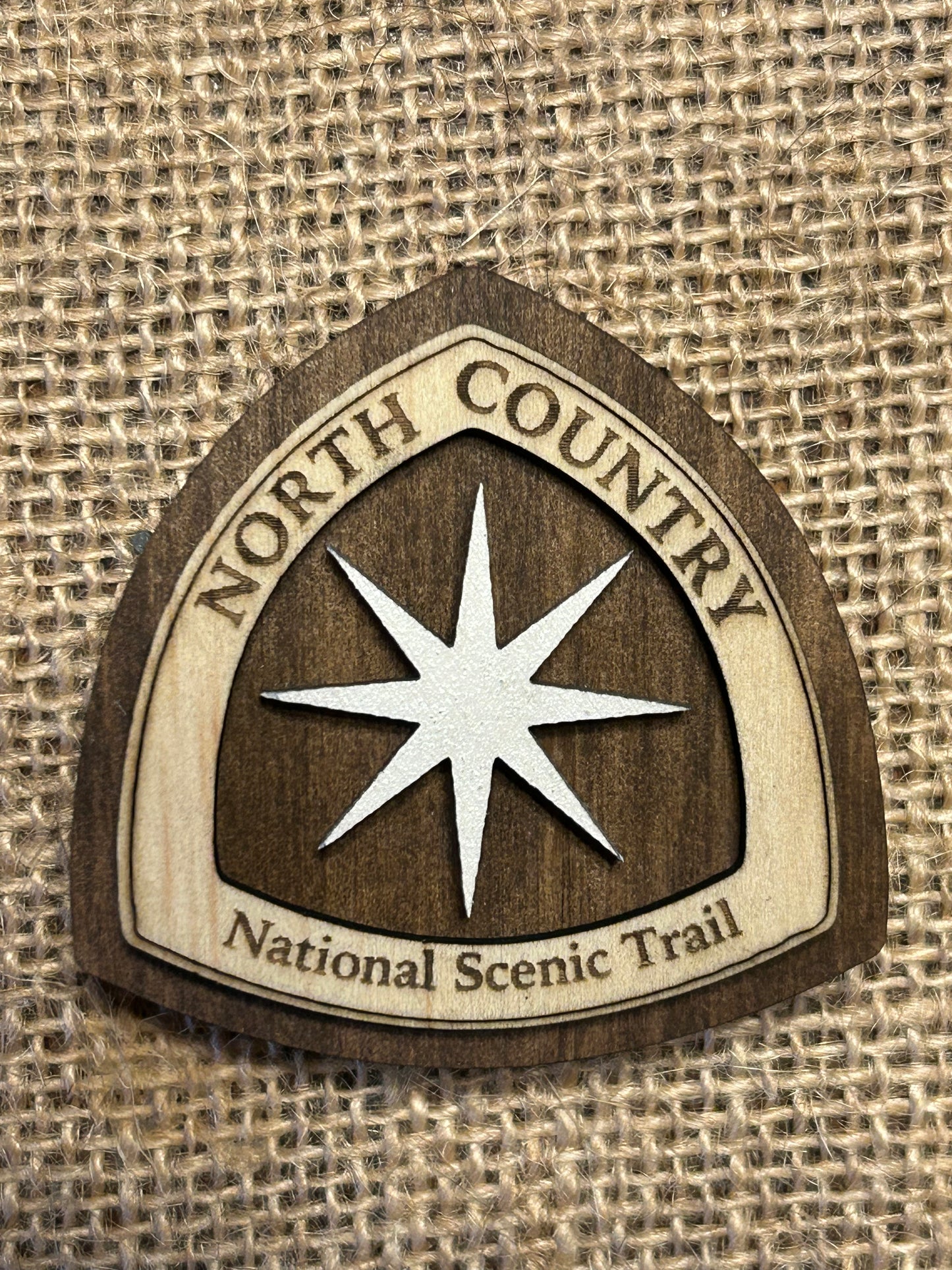 National Trail Icon with Text "North Country National Scenic Trail" and a White Polaris Star Icon on a walnut-colored background.