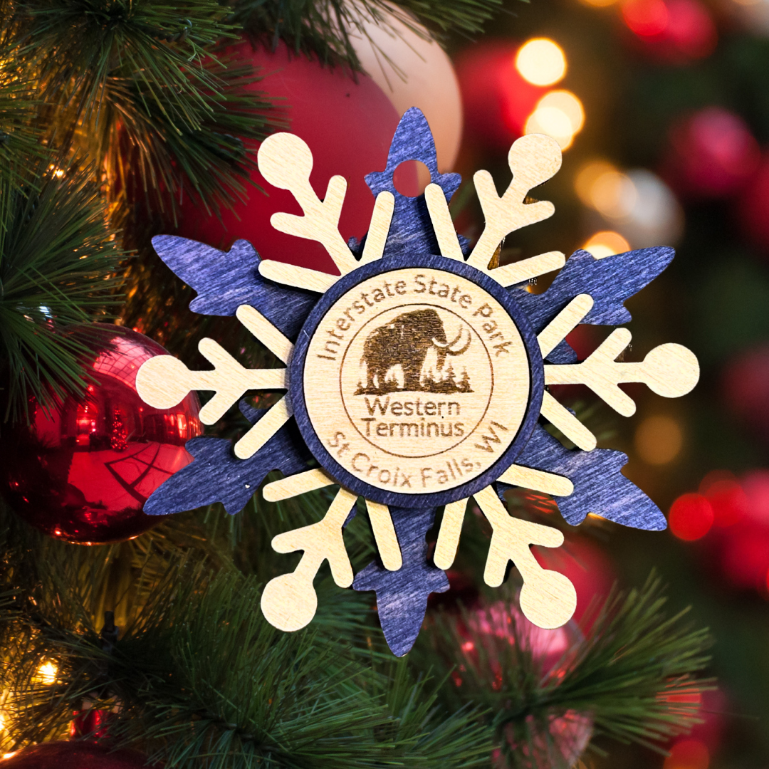Blue snowflake wood ornament depicting a woolly mammoth. Photo background: evergreen branch with lights and a ornaments.