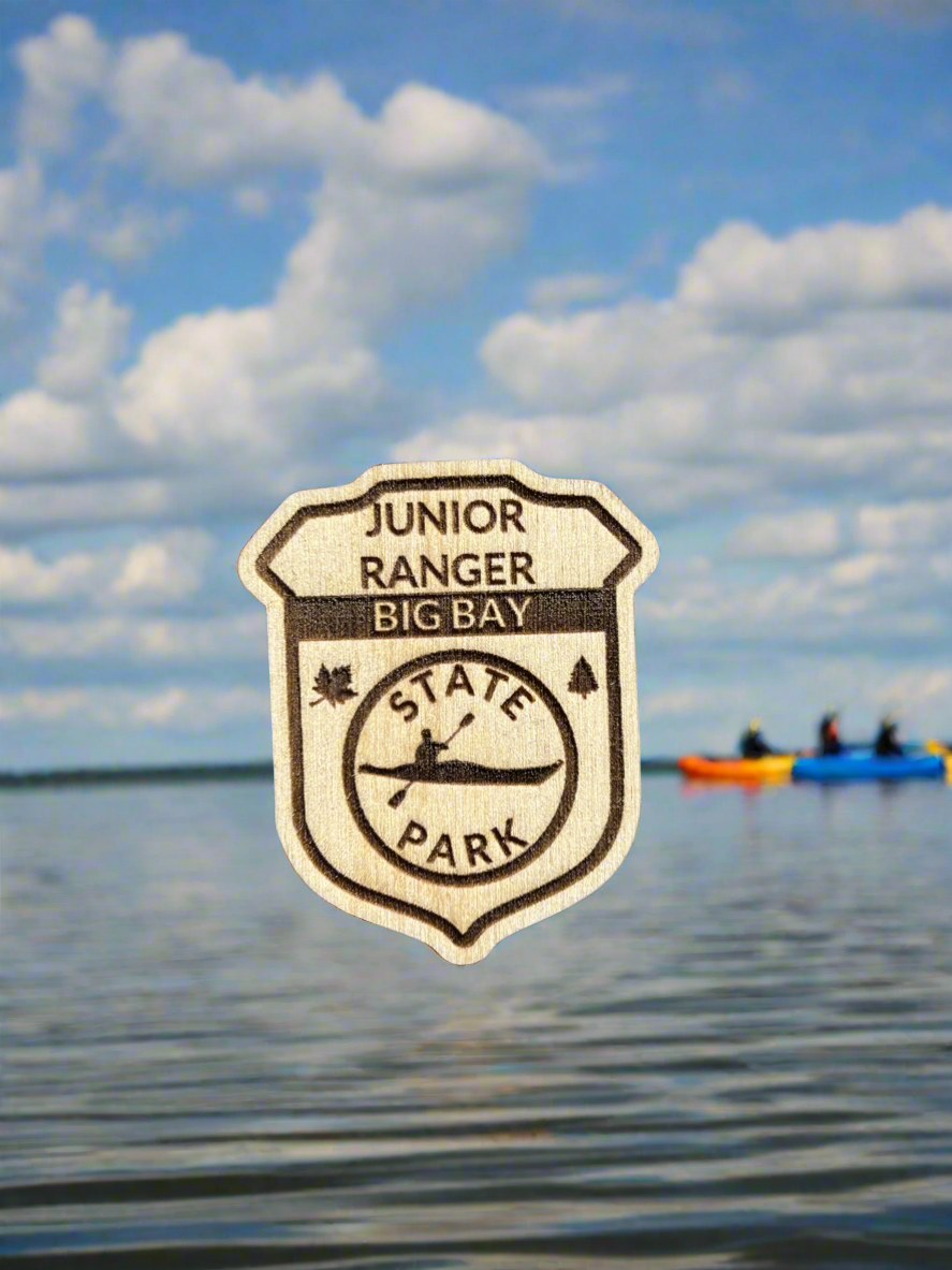 Wood Junior ranger badge depicting Big Bay State Park with a Kayak Symbol.