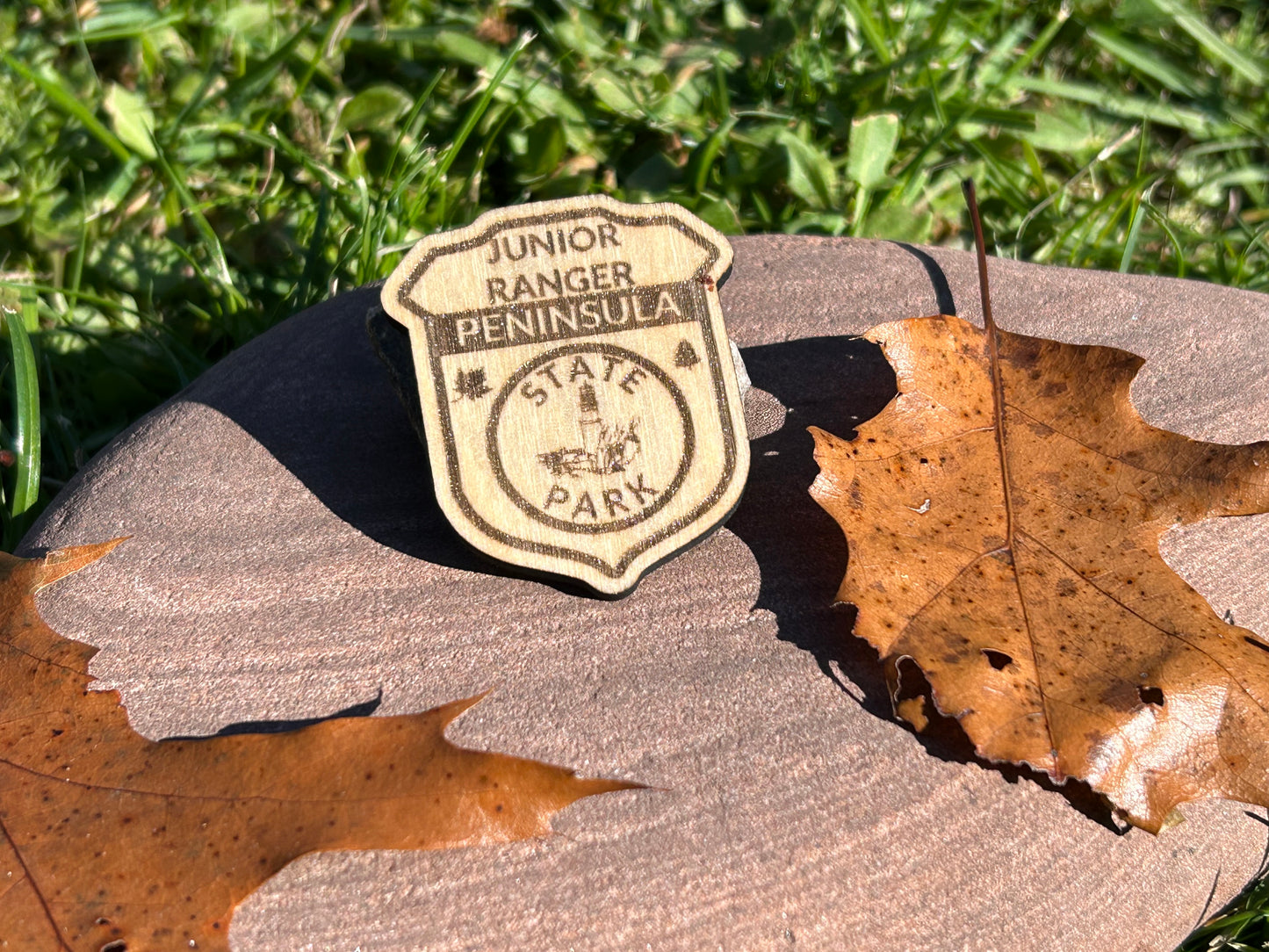 Wood badge shaped junior ranger pin with text Peninsula State Park and a lighthouse icon.