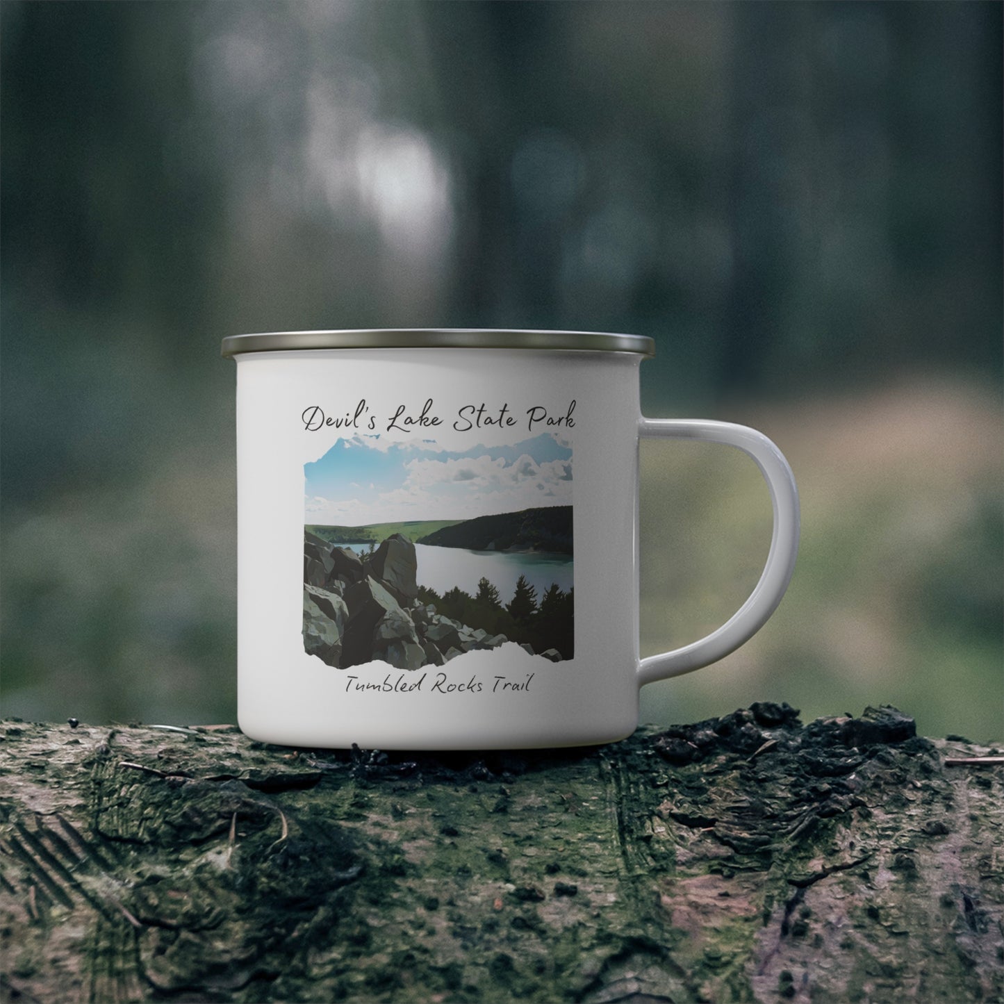 White enamel campfire mug with picture overlooking Devil’s Lake and the text Devil’s Lake State Park, Tumbled Rocks Trail. Background: mug sitting on a log in the woods.