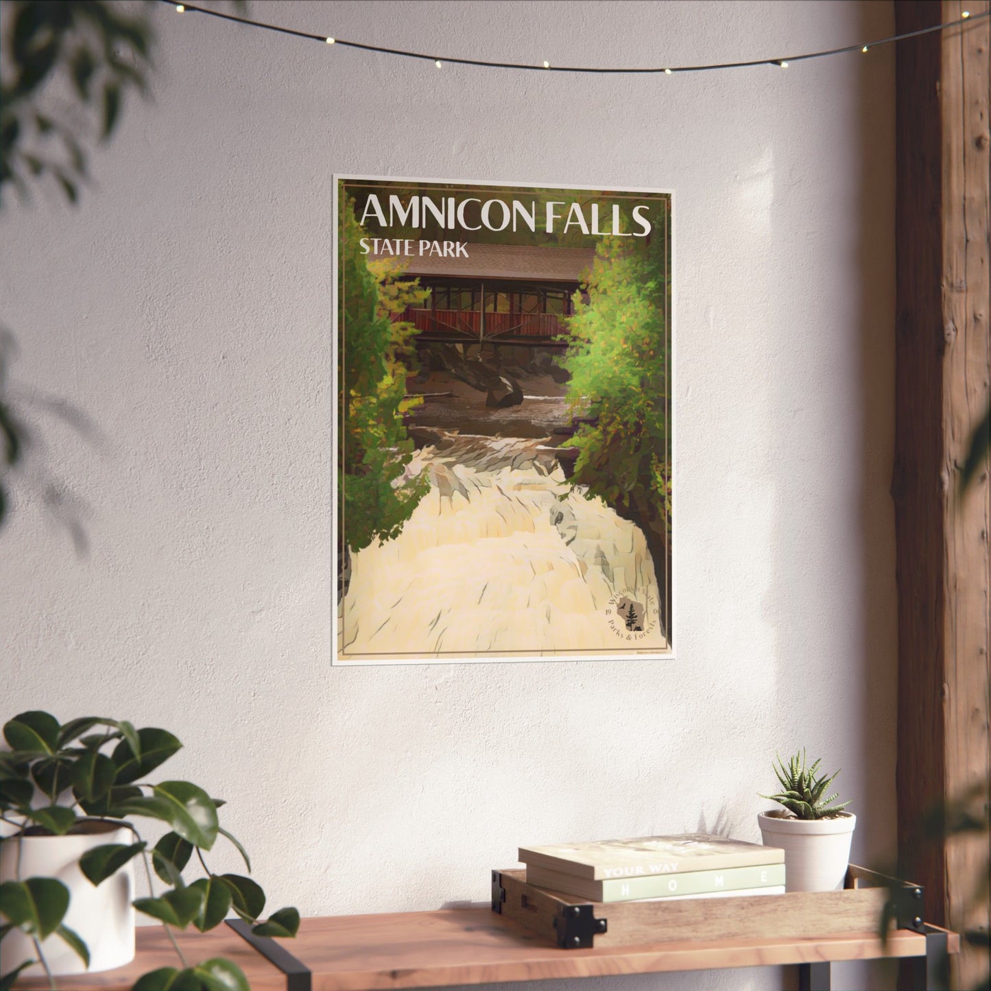 Poster featuring the Historic Horton Bridge at Amnicon Falls State Park with water rushing below it. Photo background: poster hanging on a wall above a wood shelf with books and potted plants.