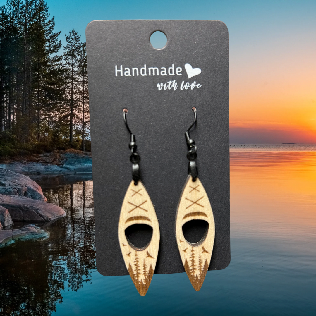 Wood kayak shaped earrings with engraved forest and birds scene. Photo background: sunset over a calm lake.
