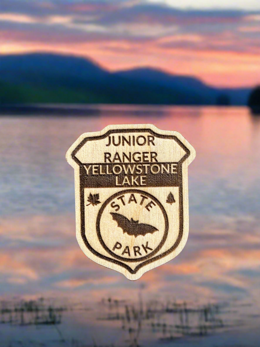 Wood badge shaped junior ranger pin with text Yellowstone Lake State Park and bat icon.