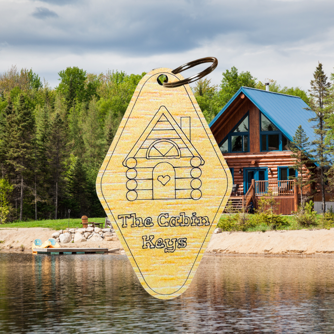 Wood grain acrylic keychains with log cabin icon and text “the cabin keys”. Photo background: log cabin nestled along the lake with a sandy beach.