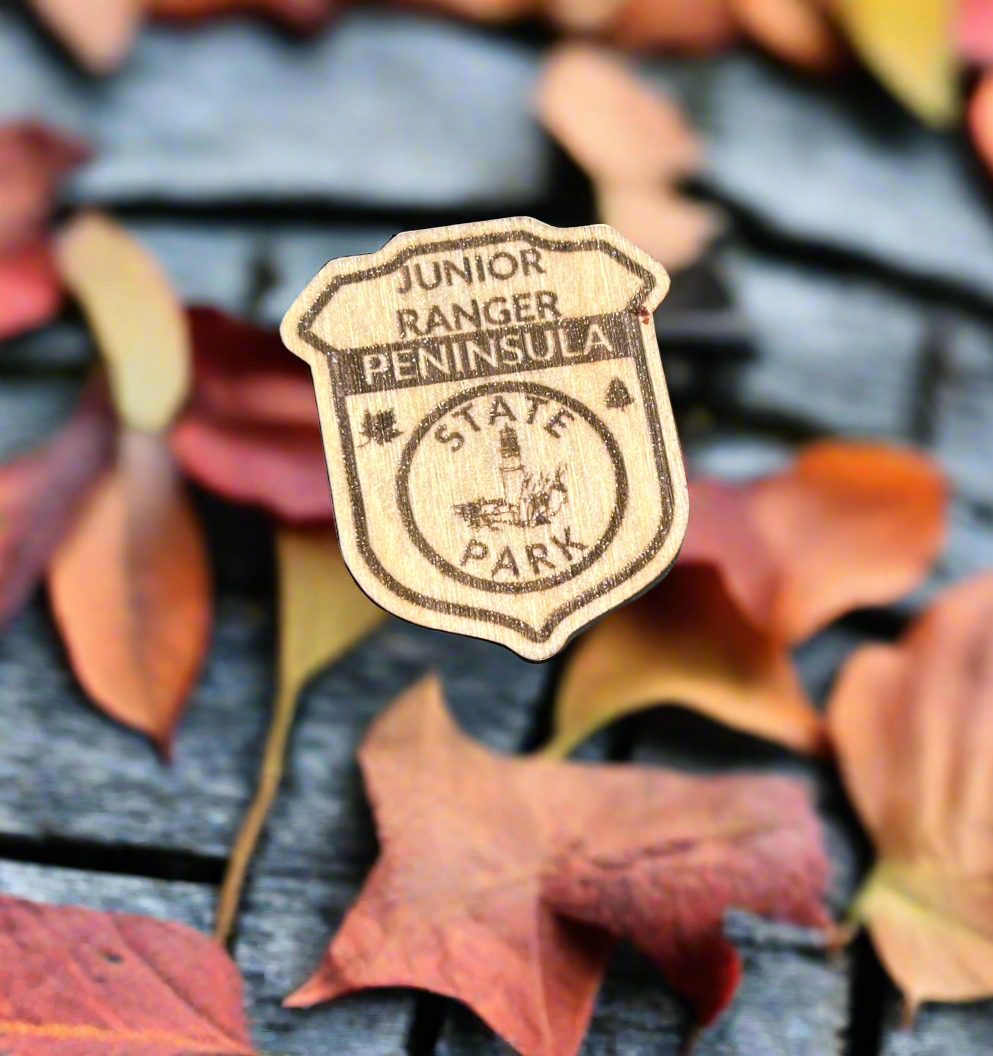 Wood badge shaped junior ranger pin with text Peninsula State Park and a lighthouse icon.