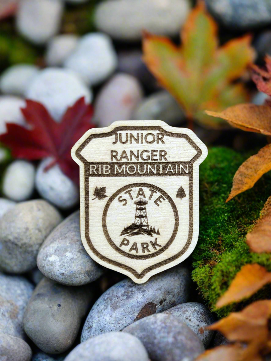 Wood badge shaped junior ranger pin with text Rib Mountain State Park and a observation tower on a hill icon.