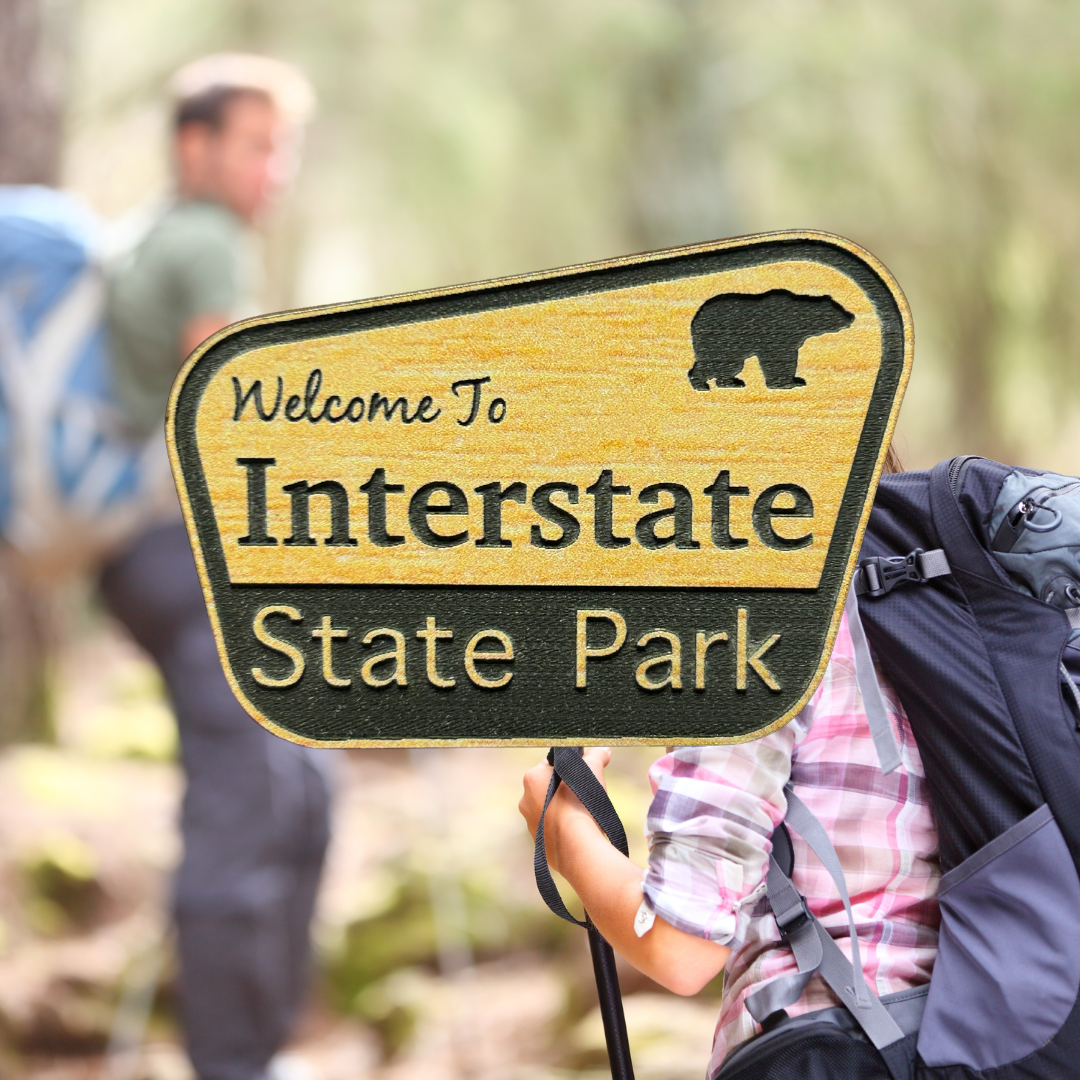 Engraved wood grain acrylic with “Welcome to Interstate State Park”. Photo background: hikers hiking through the woods.