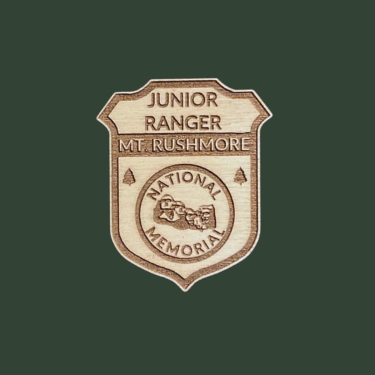 Wood Junior Ranger badge featuring an icon of Mount Rushmore with the Text: Junior Ranger Mount Rushmore National Memorial. Photo background: green background.