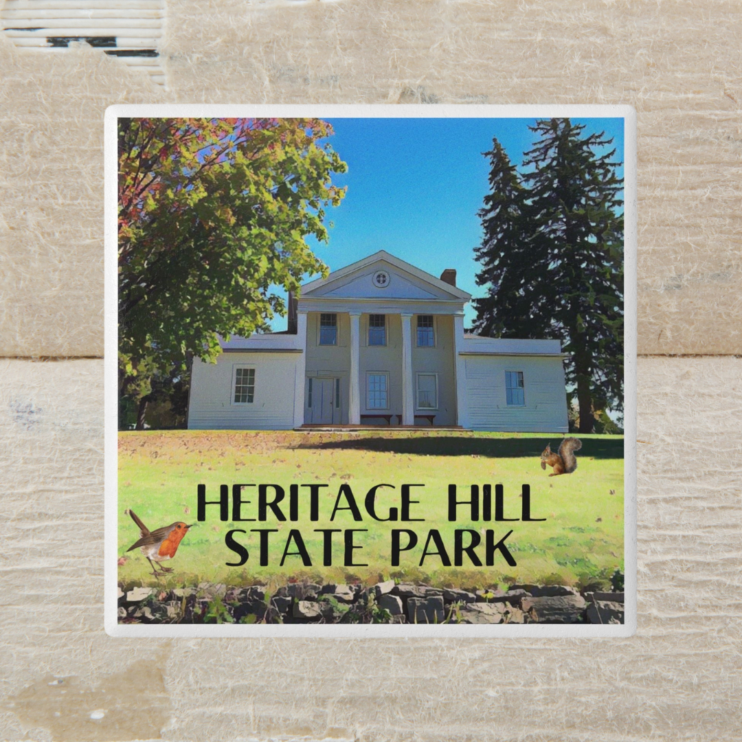 Coaster depicting a a restored historical estate house and the text “Heritage Hill State Park.” Photo background: painted wood logs.