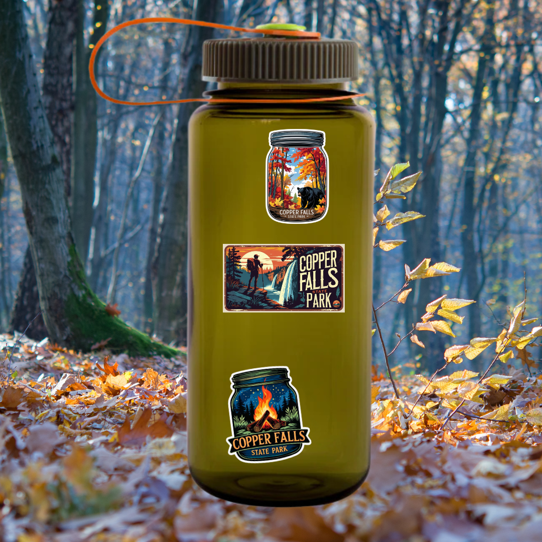 Nalgene bottle sitting on a leaf covered forest floor with 3 different styles of Copper Falls State Park stickers.
