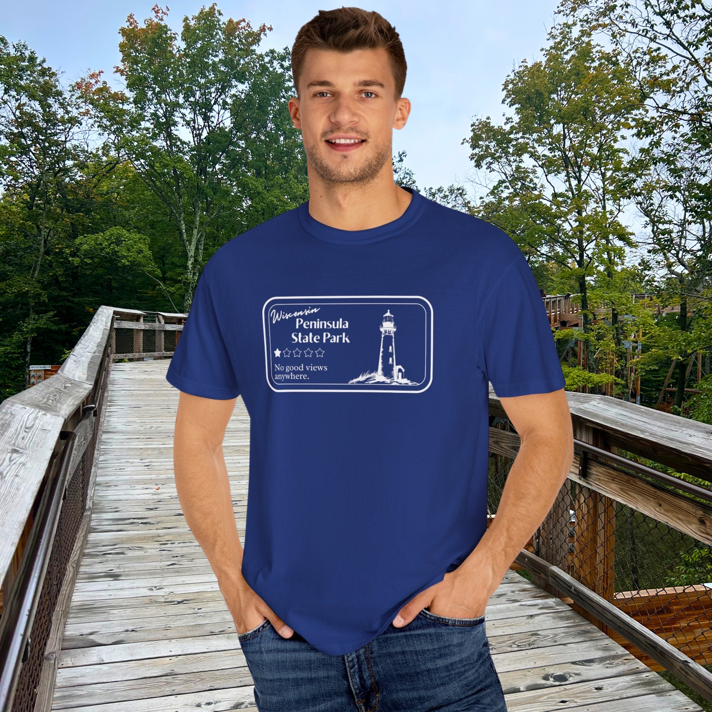 Male model wearing a Navy T-Shirt with 1 star review design of Peninsula State Park. Features a line art image of a lighthouse, 1 star graphic, and the text: “Wisconsin Peninsula State Park, No good views anywhere. Male is standing on Eagle Tower.