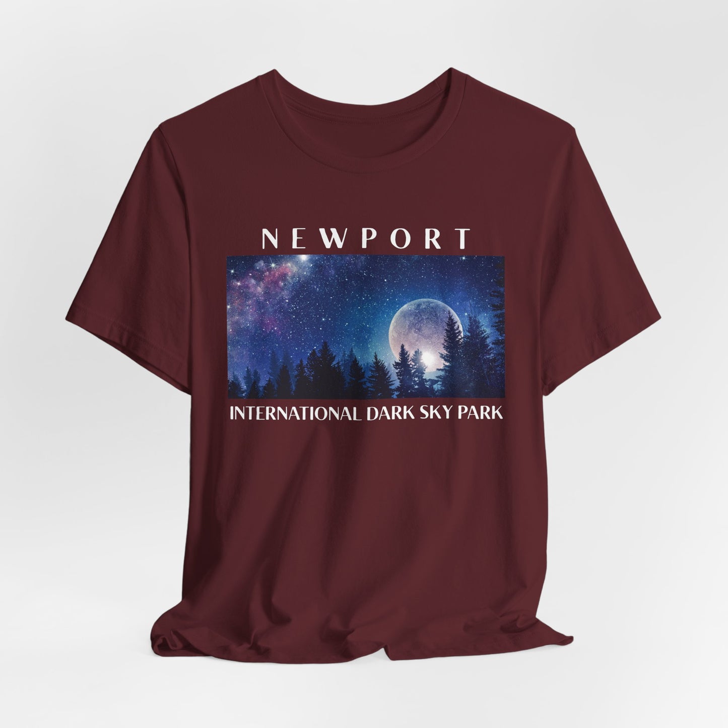Maroon t-shirt with a graphic of a night sky over trees and the text 'Newport International Dark Sky Park' on a white background.