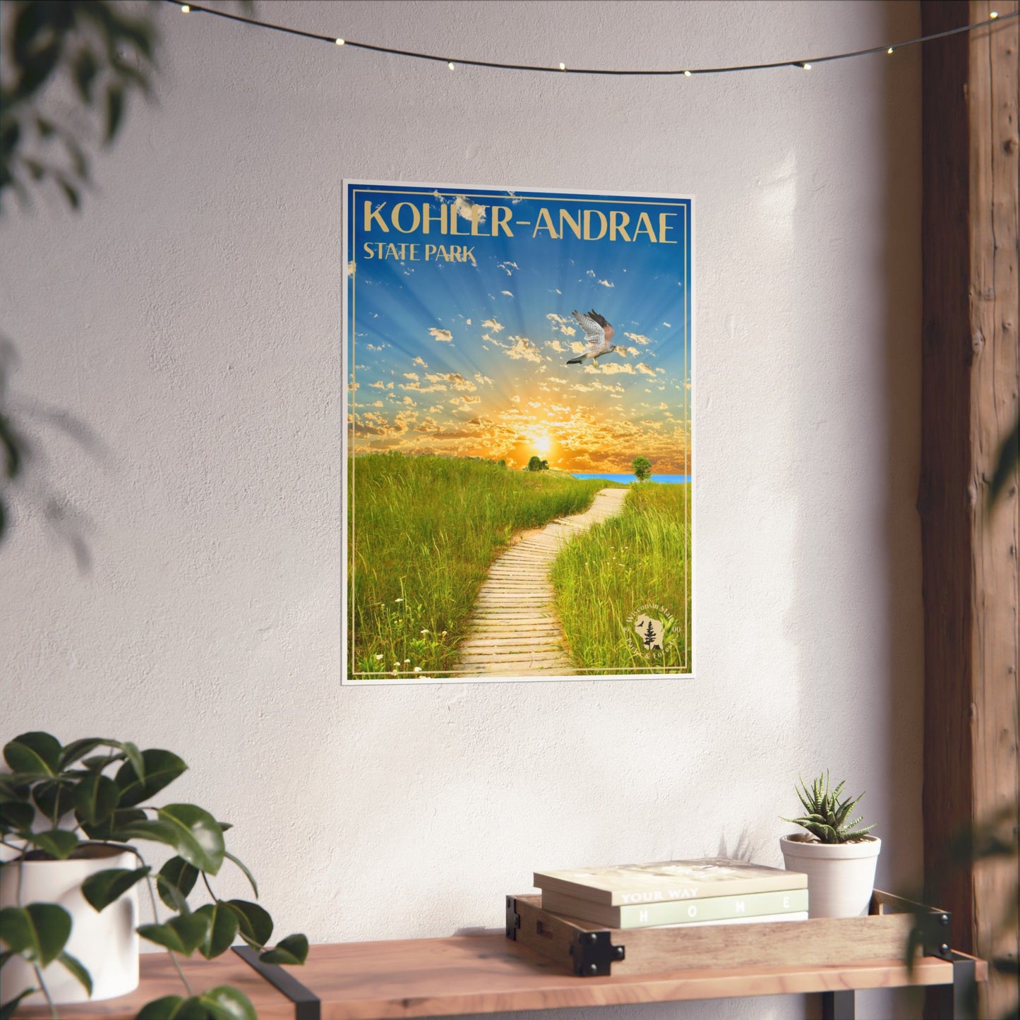 Poster featuring a vibrant sunrise over Lake Michigan and the Sand dunes of Kohler-Andrae State Park, with a Kestrel flying above.  Photo background: poster hanging on a wall above a wood shelf with books and potted plants.
