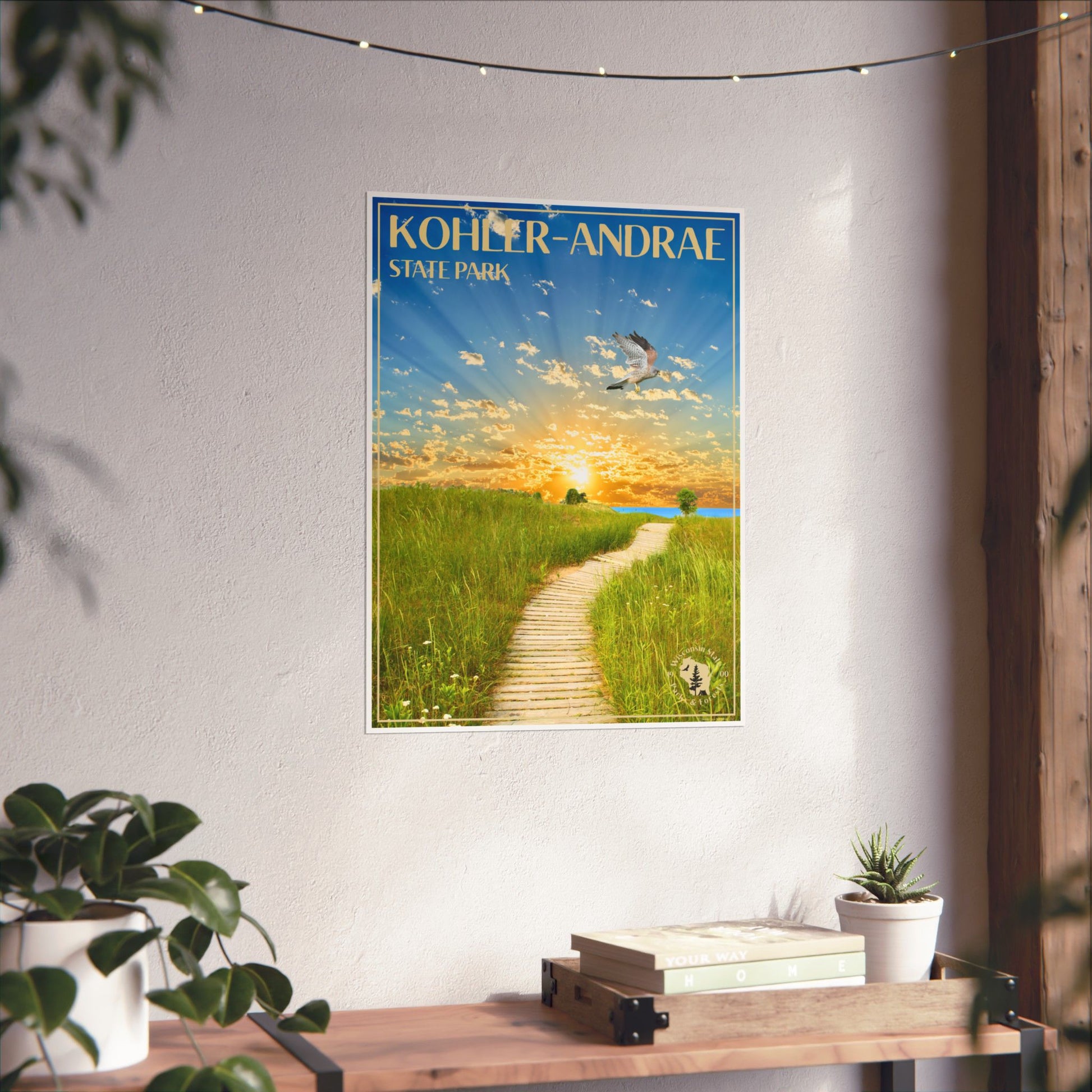 Poster featuring a vibrant sunrise over Lake Michigan and the Sand dunes of Kohler-Andrae State Park, with a Kestrel flying above.  Photo background: poster hanging on a wall above a wood shelf with books and potted plants.