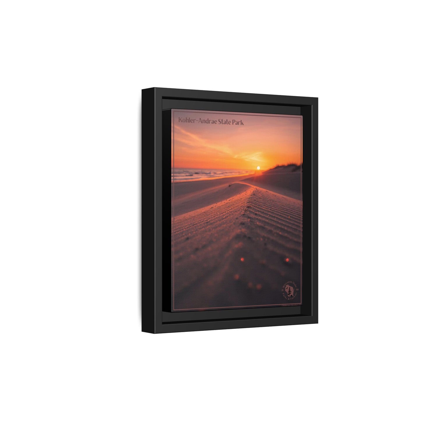 Framed wall print featuring an image of looking down a sand dune at a rising sun over a lake.