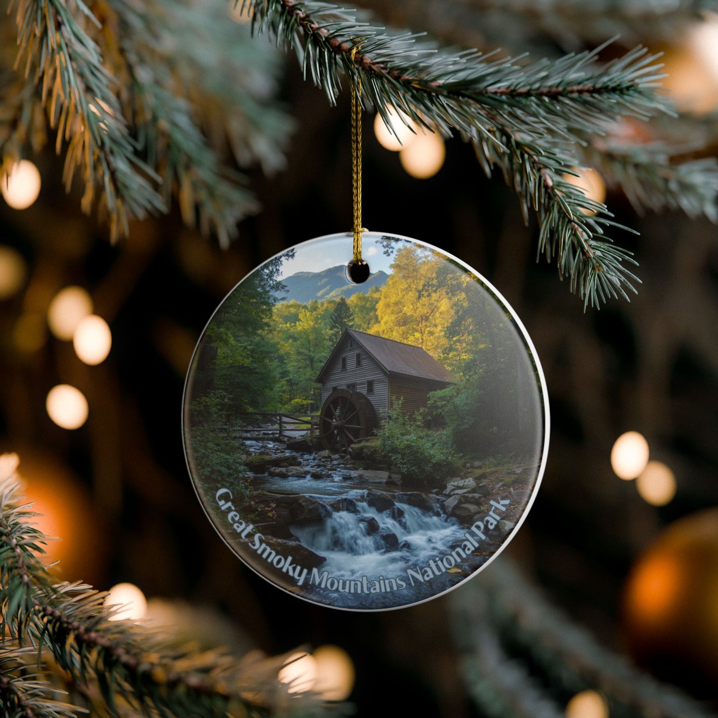 Round ornament with a scenic view of a watermill in the Great Smoky Mountains National Park, hanging on a Christmas tree.