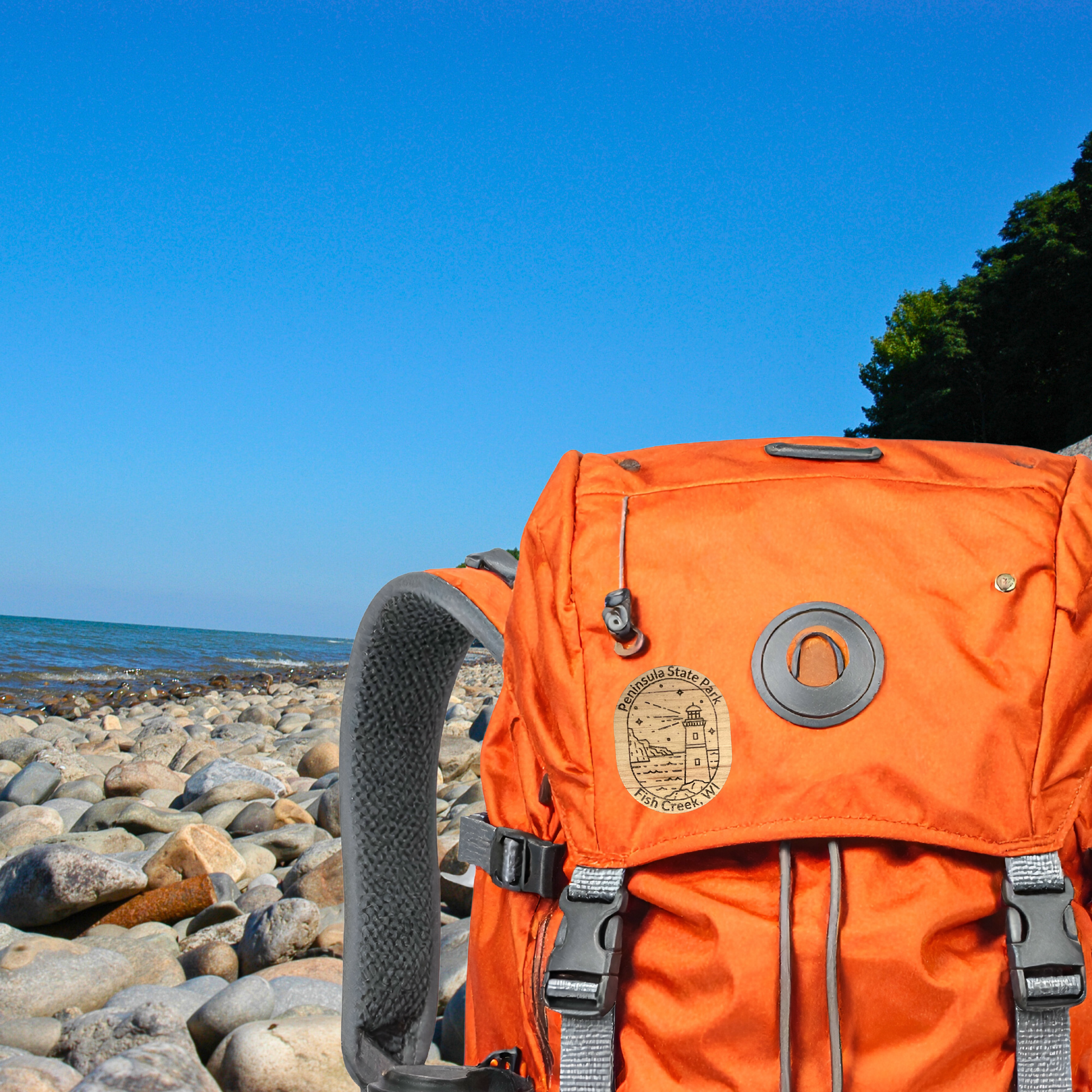 Wood Peninsula State Park pin on an Orange backpack on a rocky beach with clear blue sky