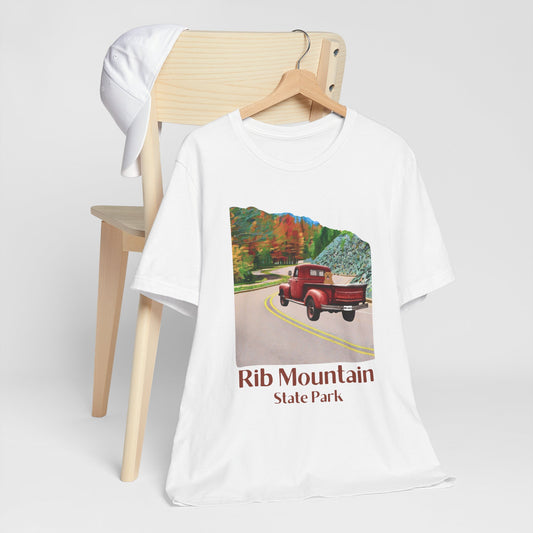White T-shirt with vintage truck driving up the road to Rib Mountain State Park during fall leaf color graphic.  Photo background: shirt hanging on a hanger from a chair
