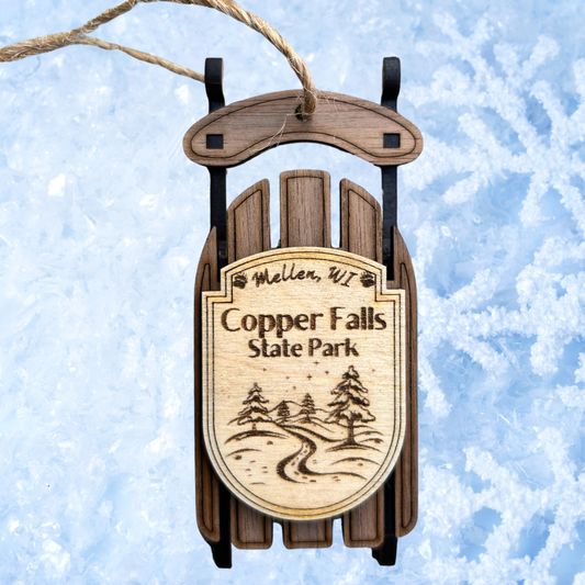 Wooden sled ornament with 'Copper Falls State Park' text on a snowy background