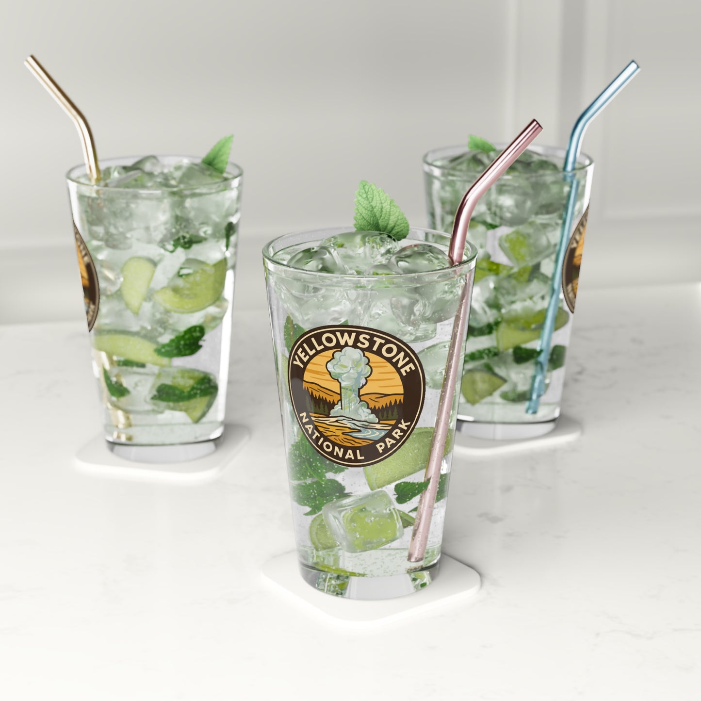 Three glasses of iced drinks with straws on a white surface, featuring a Yellowstone National Park logo.