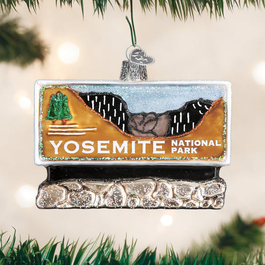 Hand painted glass ornament in the shape of Yosemite national park entrance sign on a festive background.