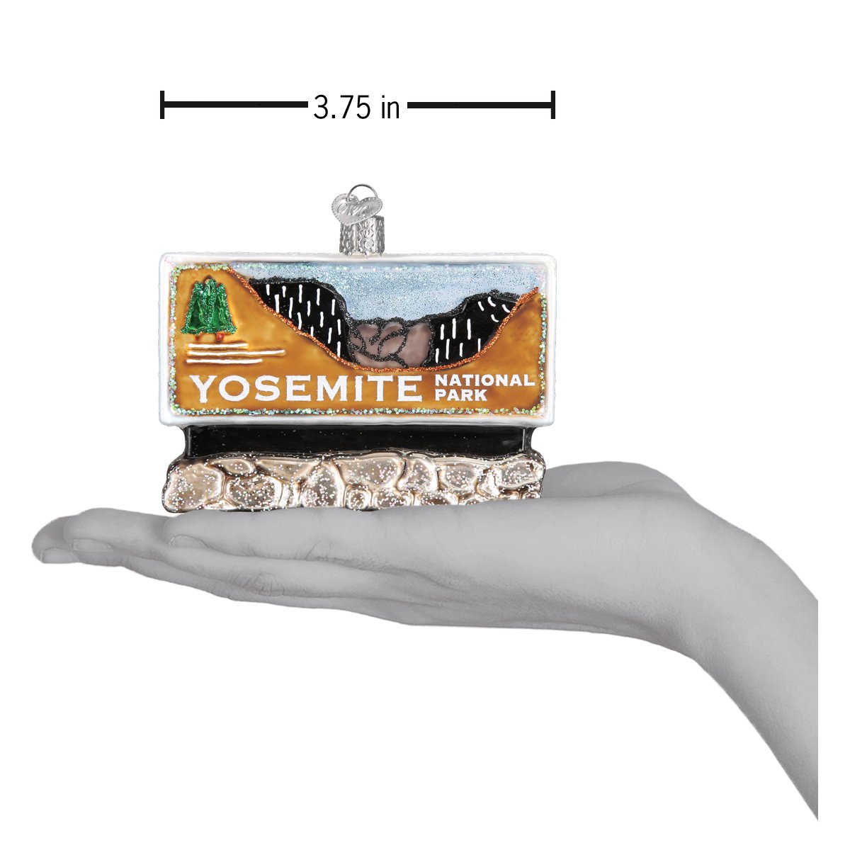Hand painted glass ornament in the shape of Yosemite national park entrance sign on a hand showing size dimensions on a white background.