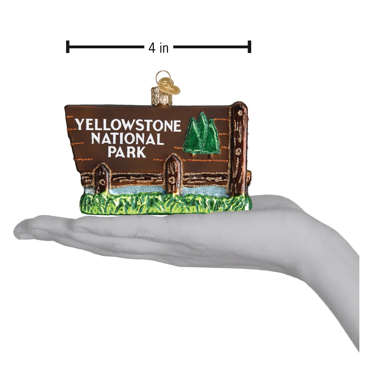 Glass Christmas ornament in shape of the Yellowstone National Park Entrance sign on a hand showing dimensions on a white background. 