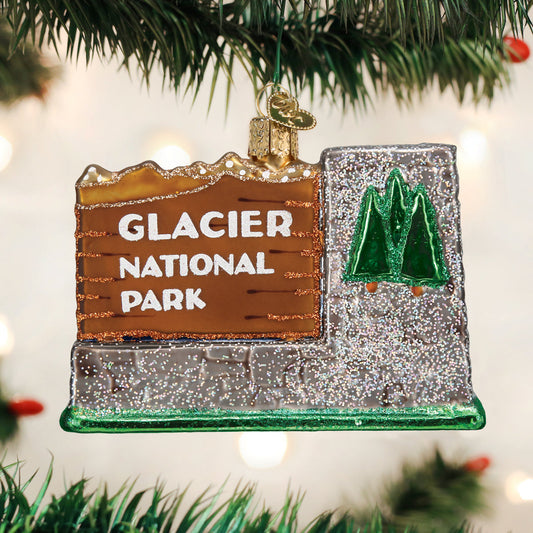 3-D glass ornament in the shape of the glacier national Park entrance sign against a festive background
