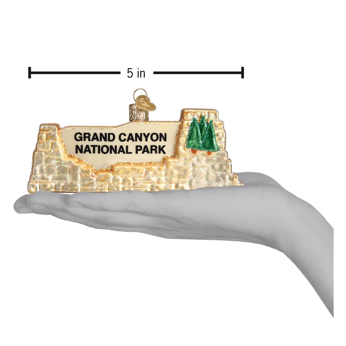 3-D glass ornament in the shape of the Grand Canyon national Park entrance sign in a hand showing dimensions against white background