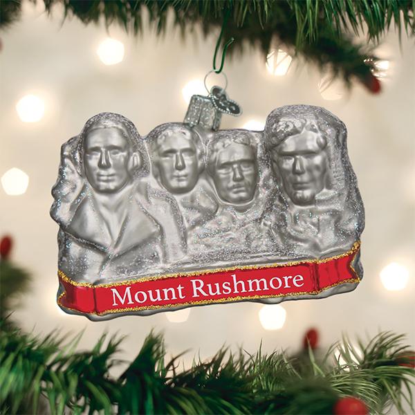 Glass ornament in the shape of Mount Rushmore on a festive background.