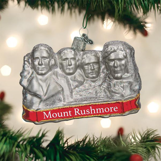 Glass ornament in the shape of Mount Rushmore on a festive background.
