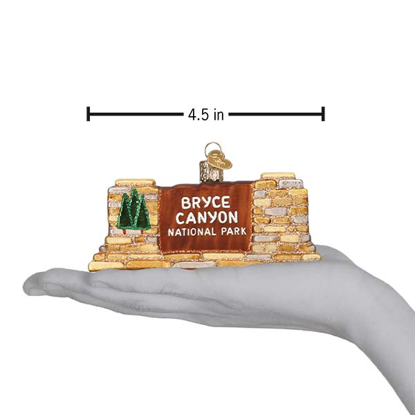 Handcrafted 3-D glass ornament in the shape of the Bryce Canyon national Park entrance sign on a hand showing size against a white background.