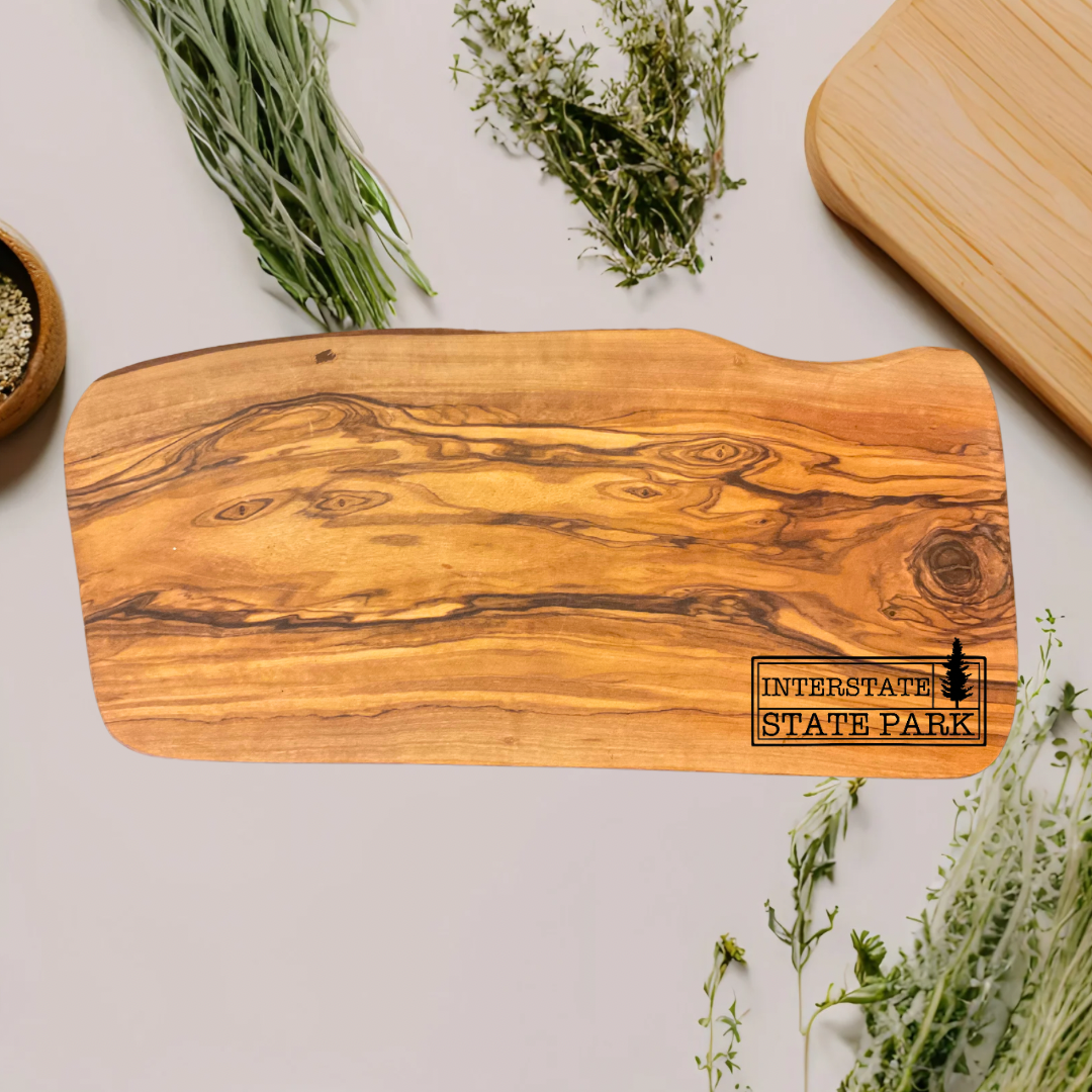 Natural olive wood board with Interstate State Park design engraved on the board.  Photo background: Counter with dried herbs.