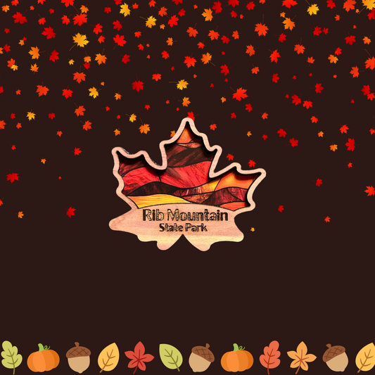 Cedar magnet in the shape of a maple leaf with a stained glass appearance and the Text “Rib Mountain State Park.”  Photo background: pumpkins, pinecones and falling leaves.