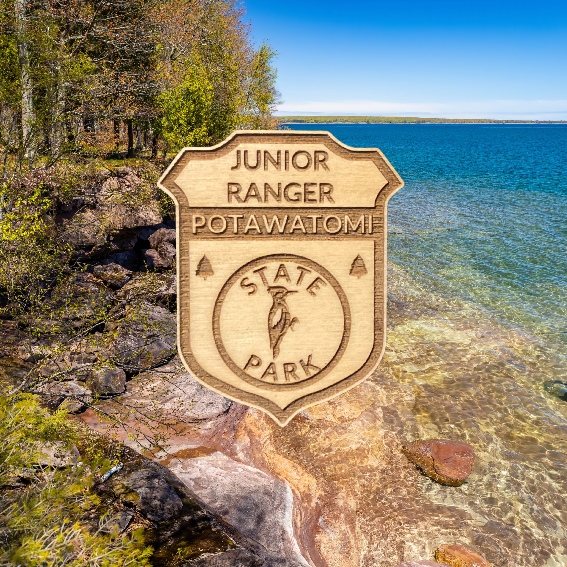 Wood badge featuring the text: “Junior Ranger Potawatomi State Park” and a woodpecker icon with a scenic background of a rocky shoreline s and trees.