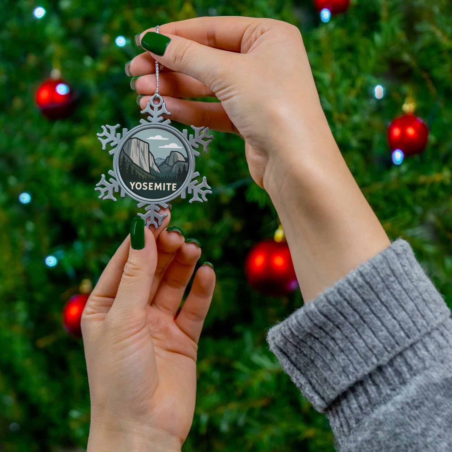 Hand holding a snowflake-shaped Yosemite ornament in front of a decorated Christmas tree.
