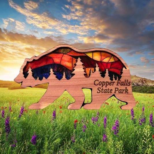 Bear shaped ornament made with cedar and a stained glass appearance.  Includes the text “Copper Falls State Park”.  Photo Background: Lush meadow at sunset.